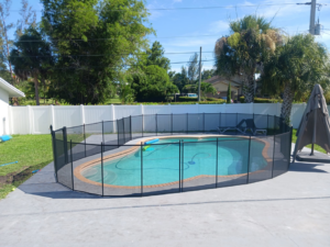 A backyard swimming pool with a newly installed black mesh safety fence by All Brand Pool Fence in Fort Lauderdale, FL.