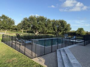 A backyard swimming pool with a newly installed black mesh safety fence by Lone Star Pool Fence in Houston, TX.