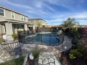 An overview of a backyard pool with a black mesh safety fence installed by Golden State Baby Barrier in Sacramento, CA.