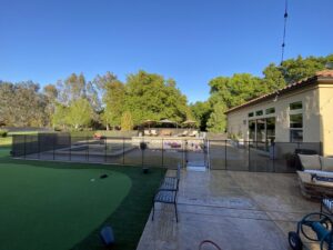 A backyard pool secured with a black mesh fence and gate, next to a putting green, by Golden State Baby Barrier in Sacramento, CA.