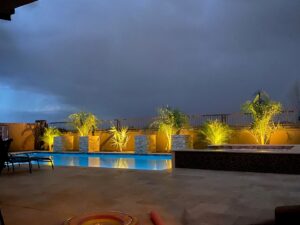 A backyard pool with accent lighting on palm trees and water features at night by Blue Magic Pools and More Inc. in Gilbert, AZ.
