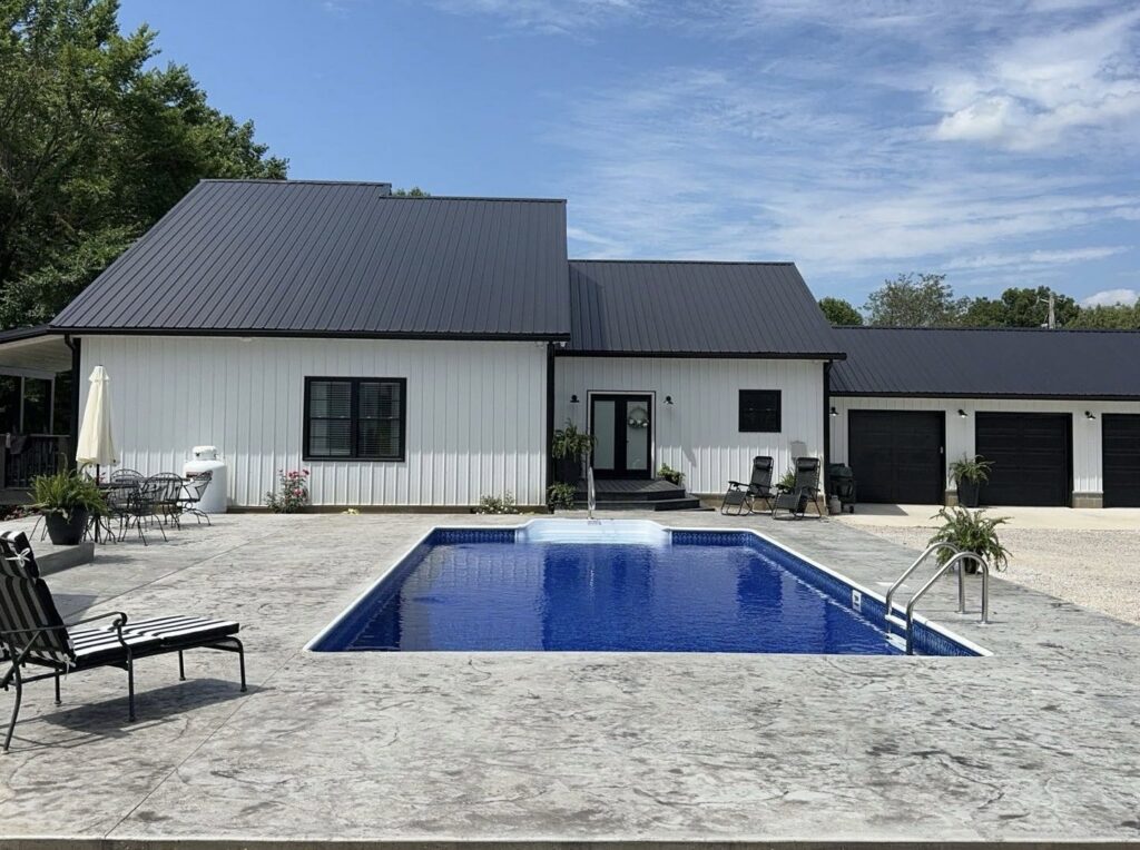 A newly completed inground pool with concrete patio next to a modern white house, built by Riverstone LLC in Bowling Green, KY.