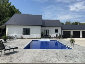 A newly completed inground pool with concrete patio next to a modern white house, built by Riverstone LLC in Bowling Green, KY.