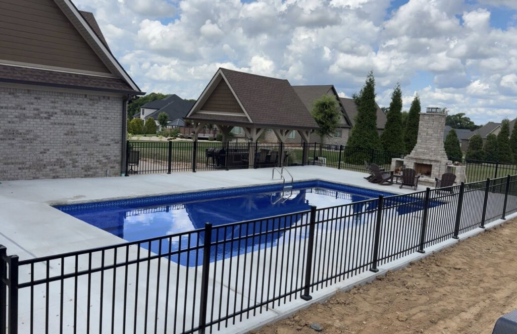 A beautiful inground pool with a dark liner, concrete patio, and stone retaining wall, completed by Riverstone LLC in Bowling Green, KY.
