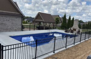 A beautiful inground pool with a dark liner, concrete patio, and stone retaining wall, completed by Riverstone LLC in Bowling Green, KY.