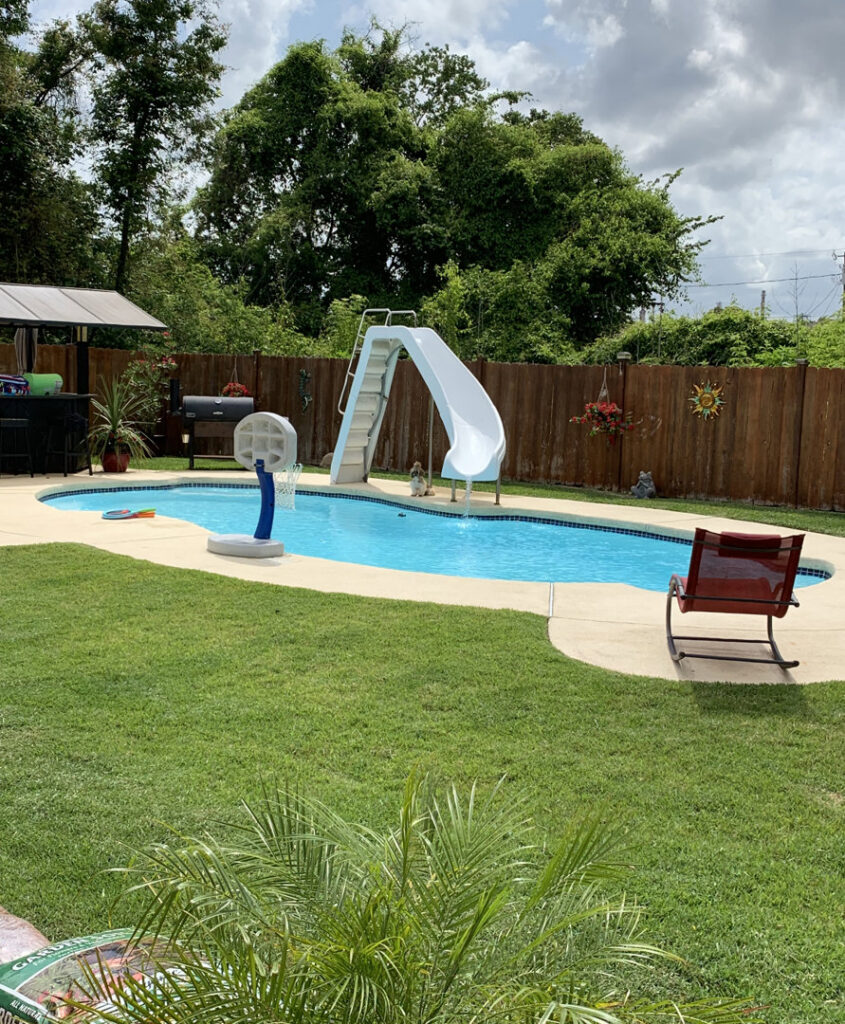 A clean, blue backyard swimming pool featuring a slide and basketball hoop, maintained by La Pool Pro LLC in New Orleans, LA.