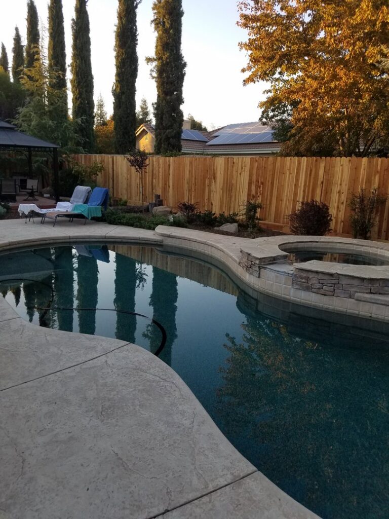 A beautiful backyard pool area enclosed by a wood privacy fence, installed by The Fence Company in Fresno, CA.