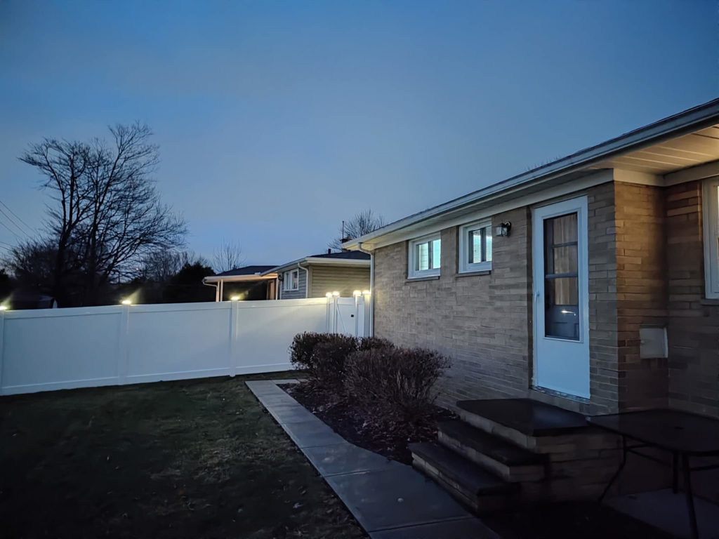 A backyard view of a white vinyl fence with integrated post lighting installed by Fence Guys INC in Cleveland, OH.