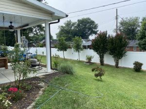 A white vinyl fence enclosing a backyard with a patio and mature trees by Nailed It Fencing and Exteriors in Evansville, IN.