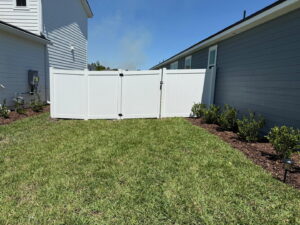 A white vinyl fence with a gate installed in a residential backyard by Top Fence LLC in Jacksonville, FL.