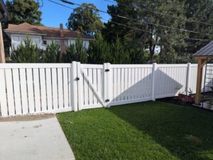 A newly installed white vinyl fence with a gate enclosing a residential backyard by American Fence Company of Norfolk in Grand Island, NE.
