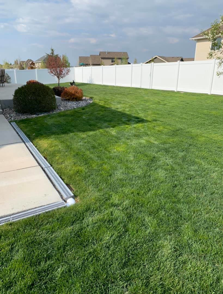 A long stretch of white vinyl privacy fence installed in a residential backyard by Highmark Landscaping in Gillette, WY.