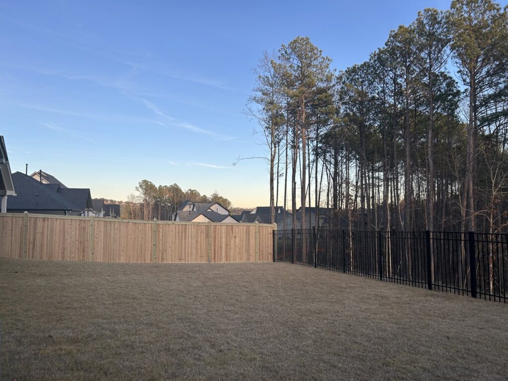 A backyard fence combining wood privacy panels and black metal sections, installed by The Fence Dudes in Birmingham, AL.