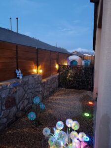 A backyard path featuring a custom wood fence on a stone wall with a gate and decorative lighting by MJ Custom Fencing in Las Cruces, NM.