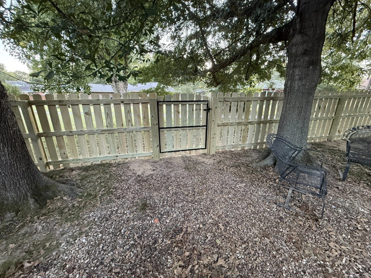 A new wooden privacy fence with a black metal gate installed in a backyard by Master Fence Builders in Fort Smith, AR.
