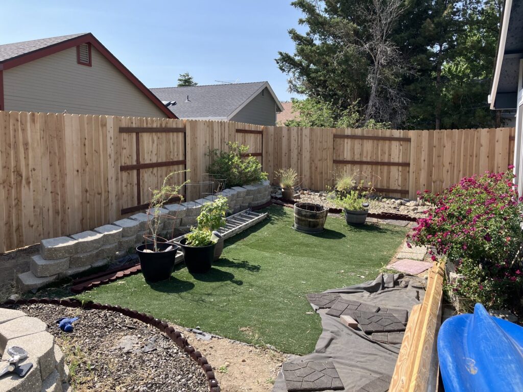 A backyard with a newly installed wood privacy fence and a stone retaining wall by This And That Fence in Reno, NV.