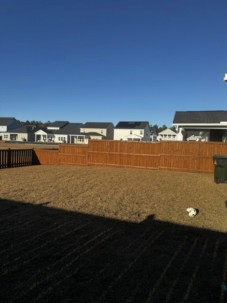 A wide view of a residential backyard featuring a well-maintained wood fence in the background by Stain and Go in Summerville, SC.
