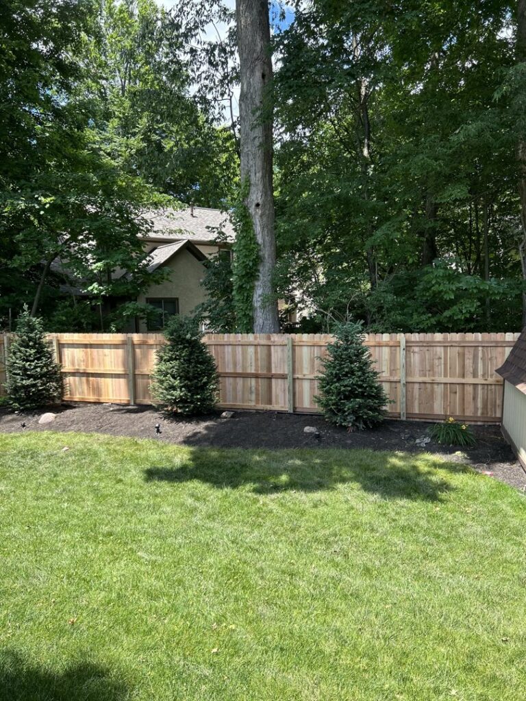 A new wood fence installed in a backyard, complemented by small evergreen trees, by ReliableFencing in Columbus, OH.