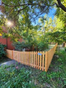 A wood picket fence with a gate installed in a residential backyard by Royal Fence & Design LLC in Olathe, KS.