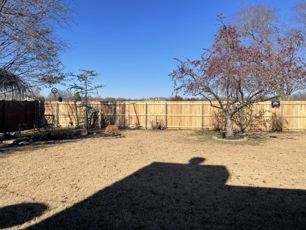 A backyard featuring a combination of new wooden privacy fence and black metal fencing installed by Ninety-One Services in Tulsa, OK