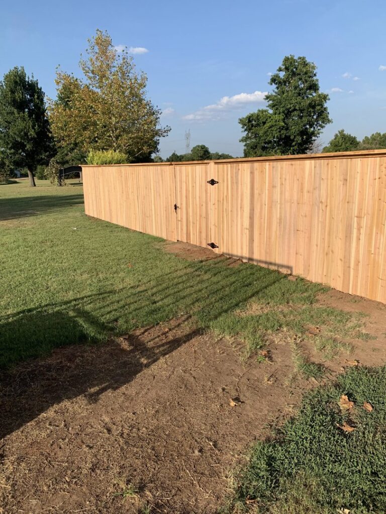 A newly installed wooden privacy fence with a gate in a sunny backyard by TOP TIER FENCE LLC in Oklahoma City, OK.