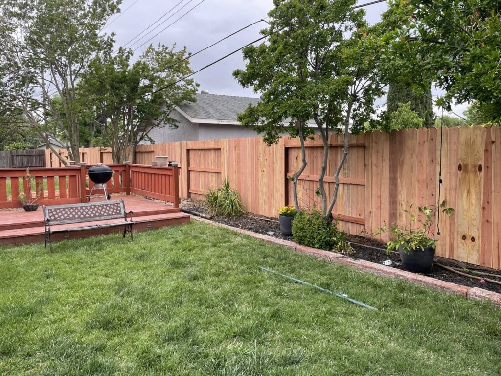 A newly installed wooden privacy fence enclosing a backyard with a wooden deck, completed by Mega Fence in Thornton, CA.