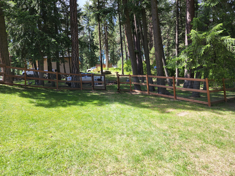 A backyard wooden fence with wire mesh and a gate, showcasing a completed project by EcoGreen Fencing in Coeur d'Alene, ID.