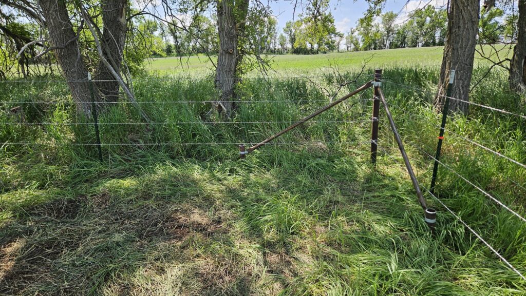 A robust barbed wire fence with a sturdy brace post in a grassy area, installed by Row Fencing and Services in Williston, ND.