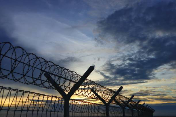 A security fence with barbed wire against a dramatic sunset sky by Palmetto Fence Co in North Charleston, SC.
