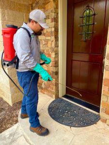 A Barefoot Mosquito & Pest Control technician using a backpack sprayer to treat around a doorway in Austin, TX.
