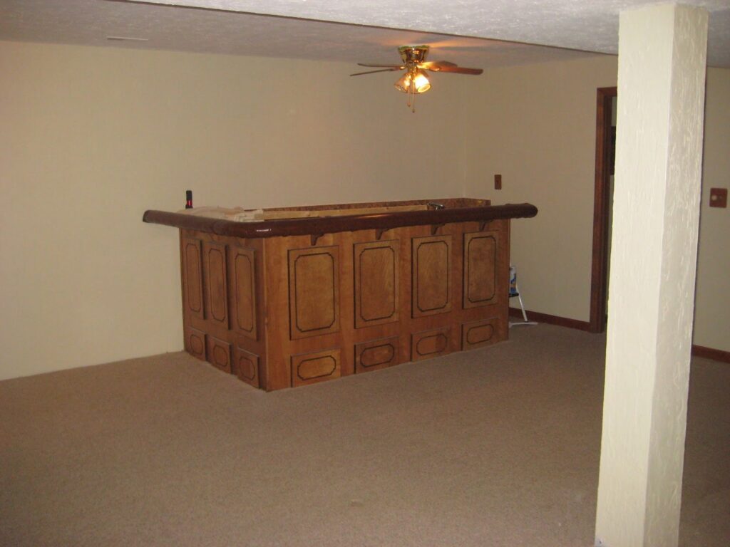 A finished basement room with newly installed beige carpet and a wooden bar area by Big Orange Country Carpets & Concepts in Knoxville, TN.
