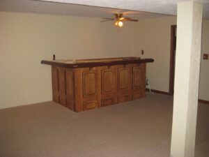A finished basement room with newly installed beige carpet and a wooden bar area by Big Orange Country Carpets & Concepts in Knoxville, TN.