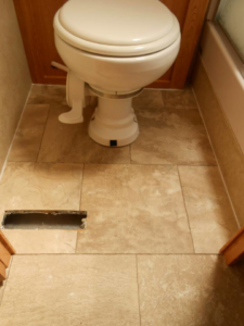 A bathroom with a toilet and newly installed light brown tile-patterned vinyl flooring by Frosty's Carpet Center, Inc. in Grand Forks, ND.