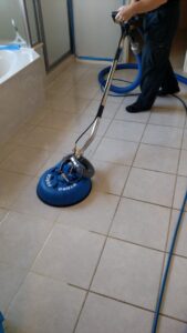 A technician cleaning bathroom tile and grout with a specialized machine for Certified Carpet Cleaning & Restoration in Skiatook, OK.