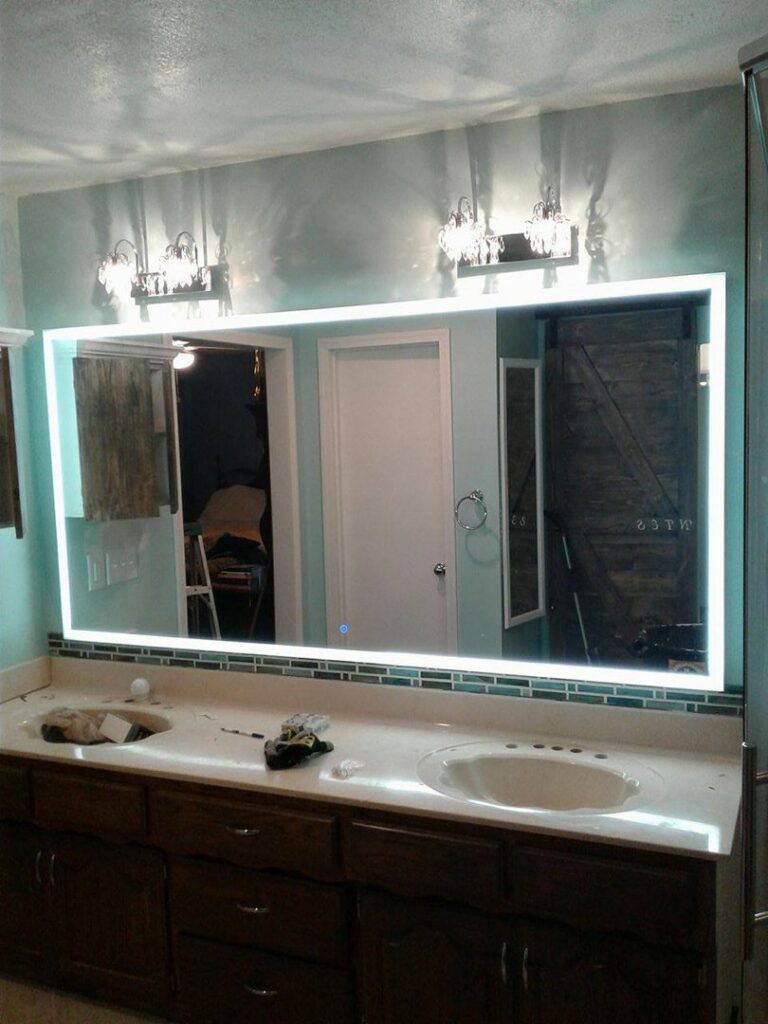 A modern bathroom vanity with a newly installed illuminated mirror and vanity lights by In the Light Electrical LLC in Kansas City, KS
