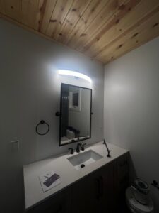 A modern light fixture installed above a bathroom vanity mirror by Llanos Electric Builders in Houston, TX.