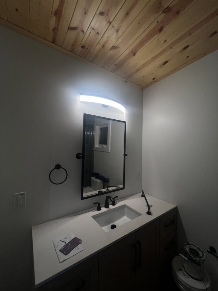 A modern light fixture installed above a bathroom vanity mirror by Llanos Electric Builders in Houston, TX.