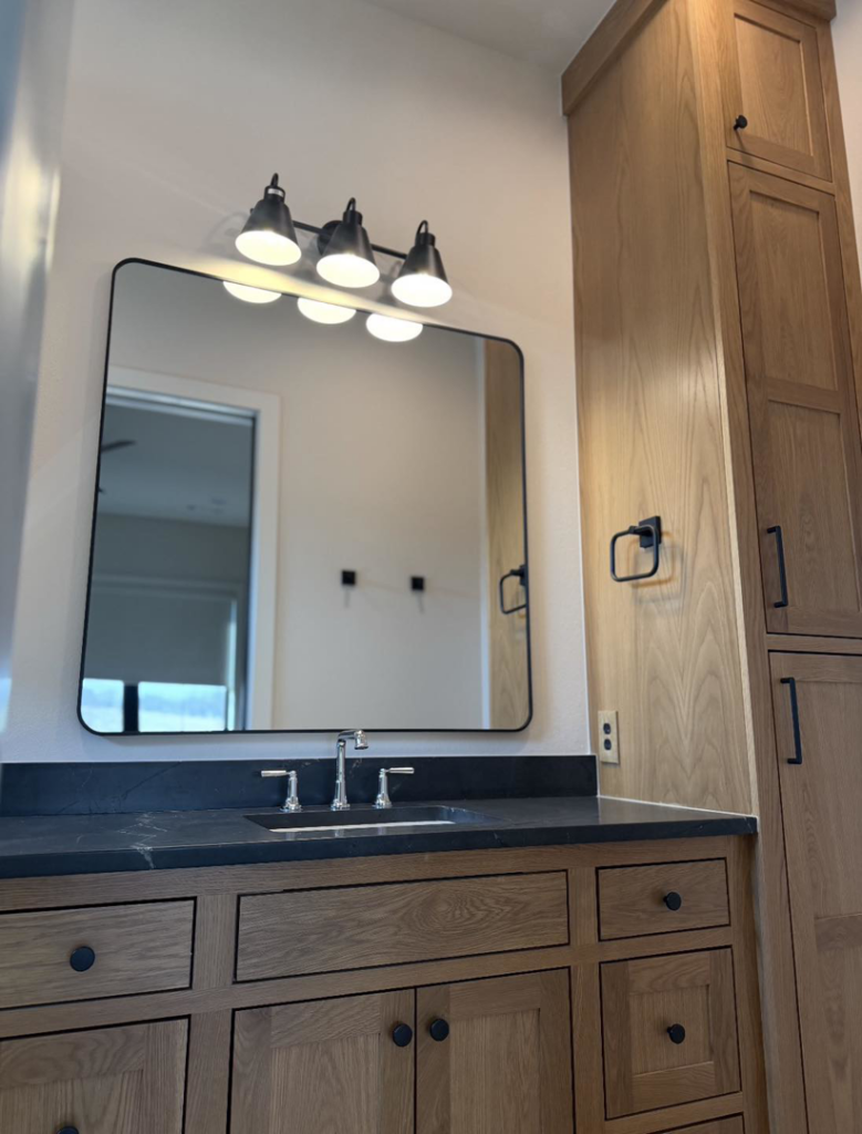 A modern bathroom vanity light fixture and electrical outlet installed by HMH Electric, serving Fayetteville, AR.