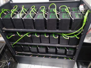 A rack of batteries with green wiring, indicating a power backup or solar installation by WM Elektries & Verkoeling in Dendron, South Africa.
