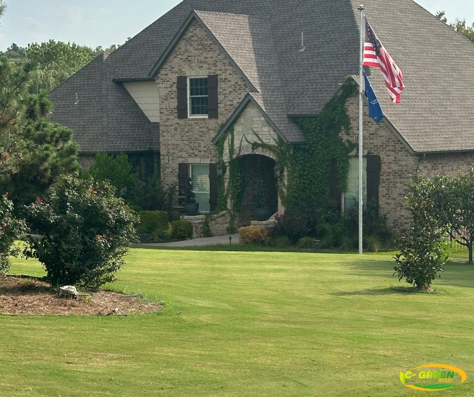 A beautiful, well-maintained green lawn in front of a residential home with an American flag by C-Green Lawns in Yukon, OK.