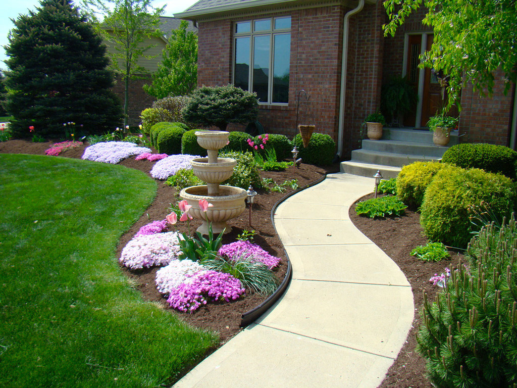 A beautifully landscaped front yard with a tiered fountain and colorful plants by Kustom Lawn Kare LLC in Greenwood, IN.