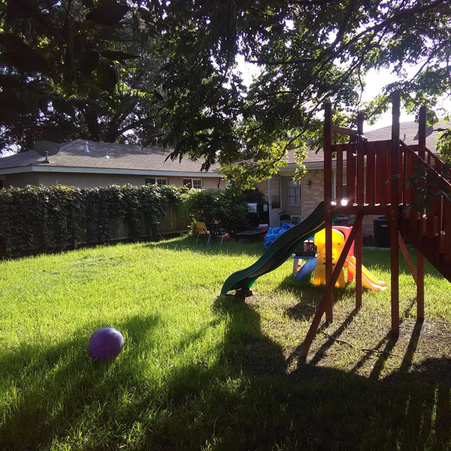 A beautifully maintained backyard lawn with a playset, showcasing quality work by DLC Service in Kenner, LA.