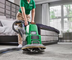 A Champion Chem-Dry technician cleaning a bedroom carpet with a professional machine in Idaho Falls, ID.