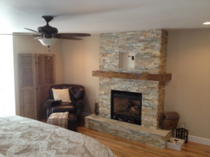 A bedroom with a newly installed ceiling fan and electrical wiring for a TV above the fireplace by Arc-n-Spark Electric in Cheyenne, WY.