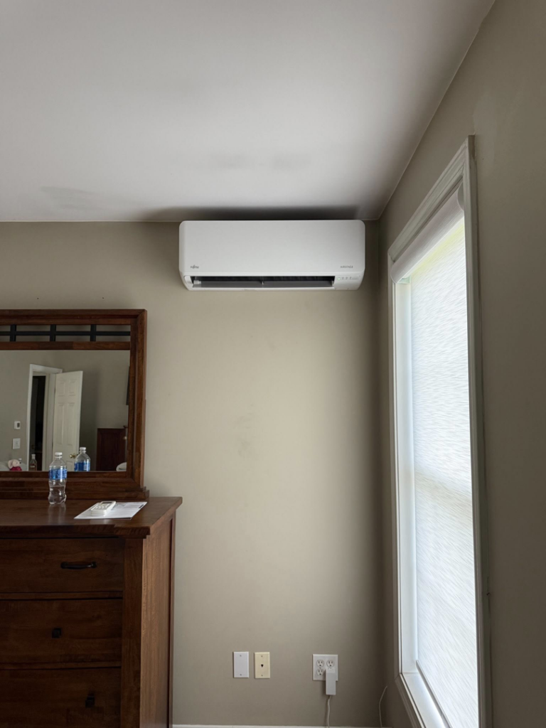 A mini-split air conditioning unit installed in a bedroom above a dresser by Precision Heating and Gas Service in Derry, NH