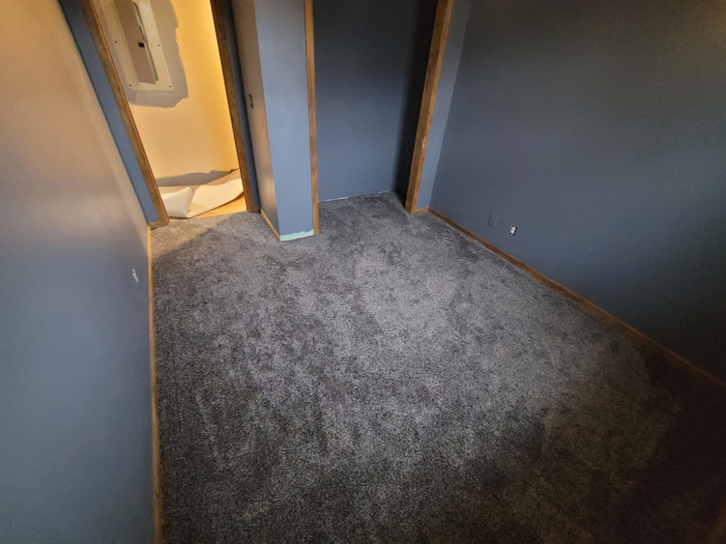 A bedroom with new grey carpet installation, showing a doorway to another carpeted area by Washington Family Flooring LLC in Bellevue, NE.