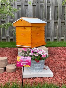 A 'Bee Friendly Zone' sign from Mosquito Authority of the Fox Valley next to a beehive, demonstrating responsible pest control in Appleton, WI.