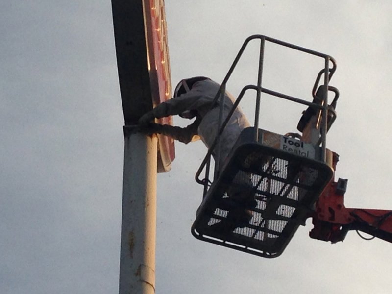 A technician in a bee suit using a lift to perform bee removal from a high sign structure for Pro-Tech Services in Corpus Christi, TX.