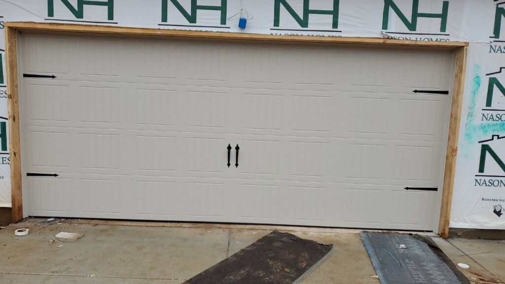 A beige garage door with decorative hardware installed on a new home by Smith's Garage Door in Clarksville, TN.