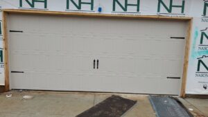 A beige garage door with decorative hardware installed on a new home by Smith's Garage Door in Clarksville, TN.